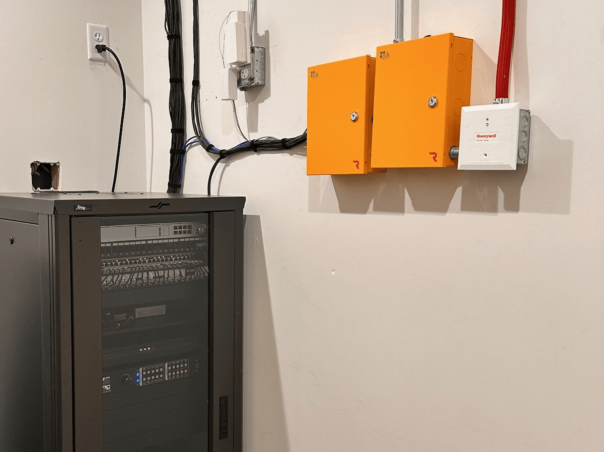 Network rack beside two access control panels in a utility room